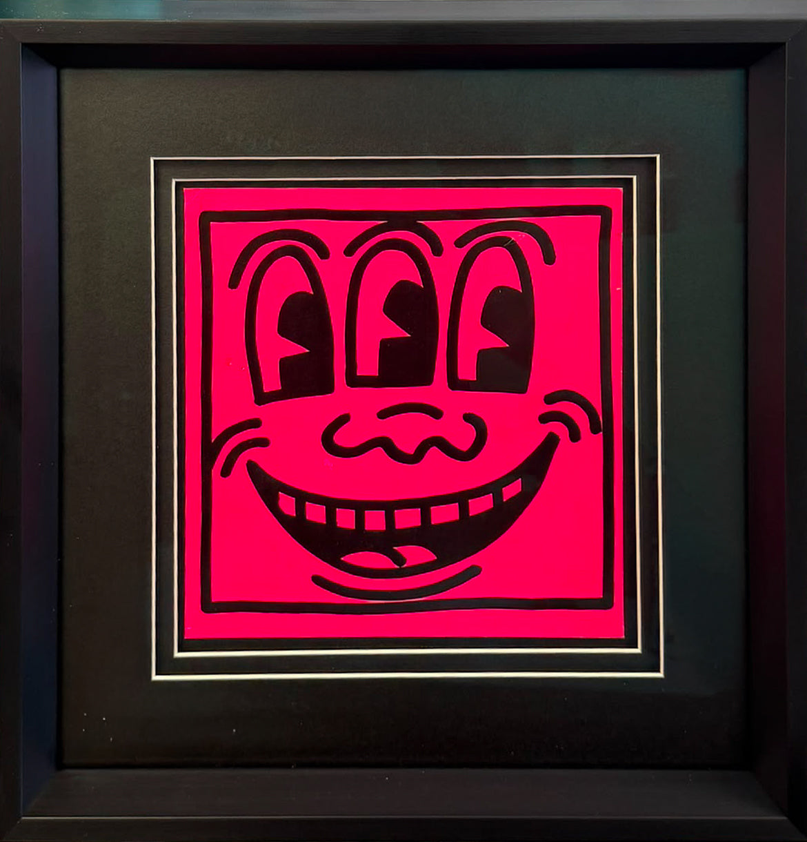 Bold black line screenprint of a grinning three-eyed face on a bright pink background