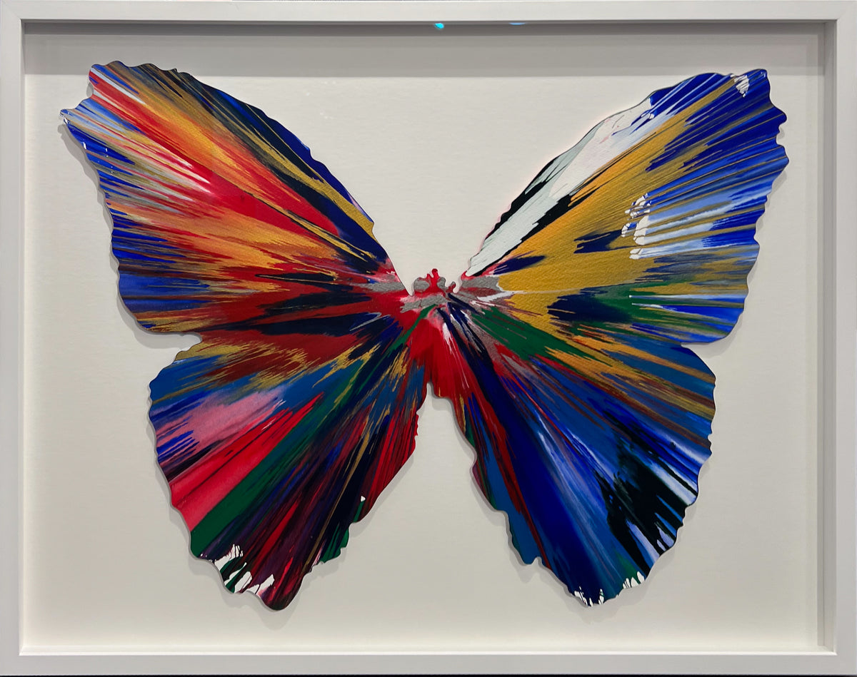 Damien Hirst butterfly-shaped spin painting in blue, red and gold, framed in white, at Creed Gallery, Ascot