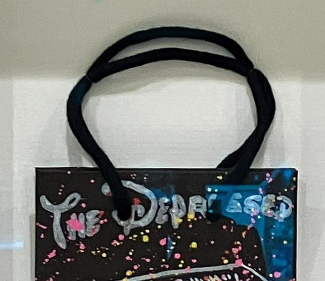 Detailed view of the top section of the Molton Brown edition, focusing on the hand-painted "The Depressed Generation" typography and the black bag handles. This contemporary mixed-media work is housed in a 24 x 37.5 cm white box frame.