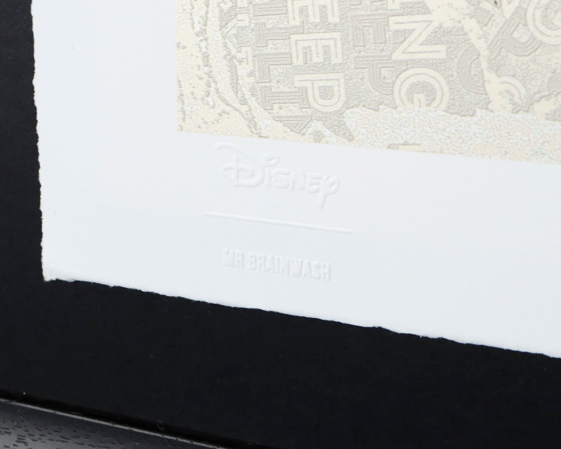 A detailed view of the bottom corner of the "Forever Mickey" print, showing the official Disney and Mr. Brainwash studio stamps and the artist's hand signature. The image highlights the quality of the fine art paper and the sleek black contemporary frame.