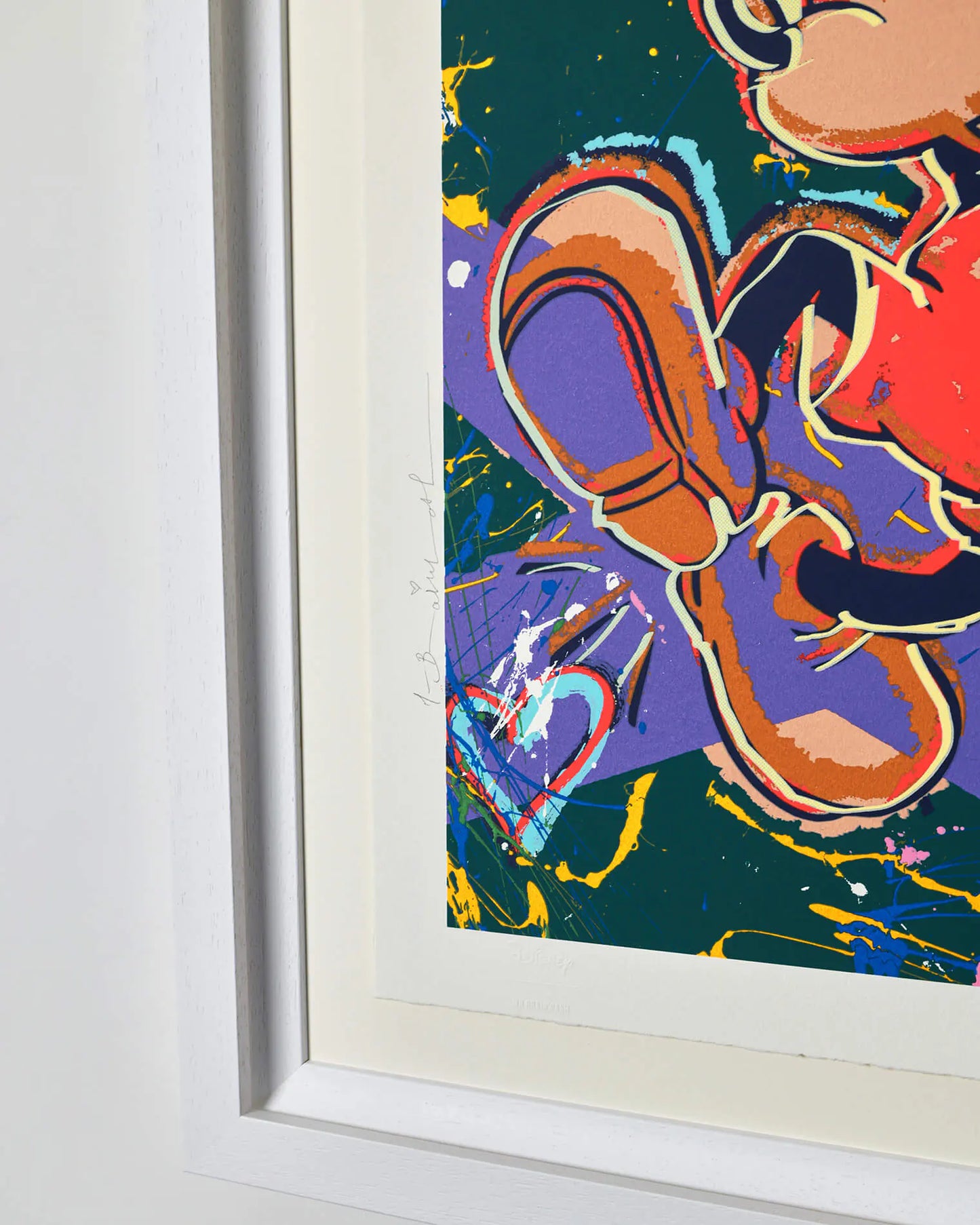 A side-angle view of the "Living the Dream" limited edition print by Mr. Brainwash, showcasing the depth of the white contemporary frame. The image highlights the textured paint splashes and rich street-art inspired colours of the official Disney collaboration.