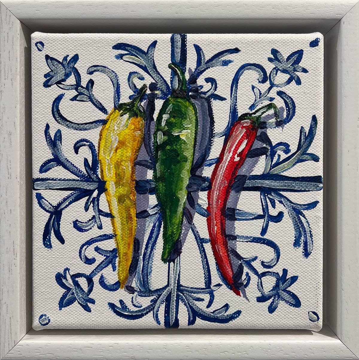 Painted still life of a yellow, a green and a red chilli on a blue and white Mediterranean tile, in a white frame