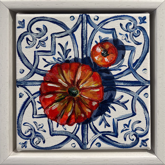 Painted still life of a large ribbed tomato and a small tomato on a blue and white Mediterranean tile, in a white frame